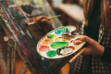 Palette with paints close-up in the hands of a girl, art school, teaching modern art