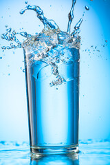pour clear water into a glass with chunks of pure real ice on a blue gradient background