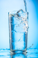 pour clear water into a glass with chunks of pure real ice on a blue gradient background