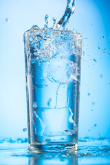 pour clear water into a glass with chunks of pure real ice on a blue gradient background