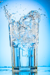 pour clear water into a glass with chunks of pure real ice on a blue gradient background