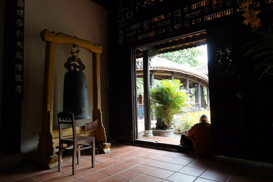 Hoi An, Vietnam, February 21, 2020: Bell and monk sitting at the door at Chùa Chúc Thánh temple. Hoi An, Vietnam