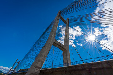 Obraz premium Cable suspension bridge over reservoir with sunstar
