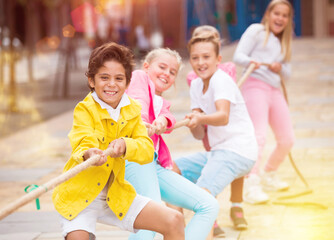 Cheerful children are competing and tug of war on the playground.
