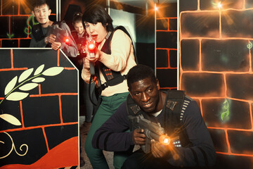 Fototapeta na wymiar Portrait of emotional multiracial couple with laser guns having fun on dark lasertag arena. Focus on woman