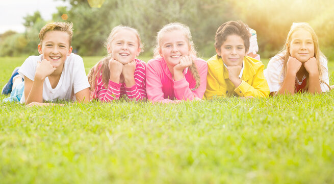 Portrait of five kids who are walking and posing lying in the park.