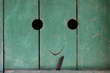 two holes and a knot on a green wooden door making a smile