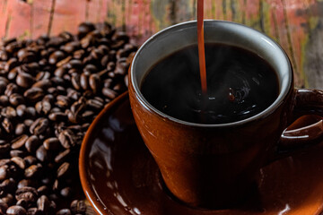カップに注がれる湯気の立つ熱いコーヒーとテーブルに散らばったコーヒー豆