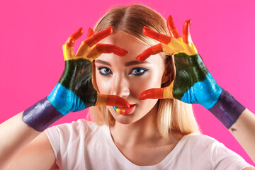 beautiful blue-eyed girl with lips and hands painted in the colors of the rainbow. looking through the heart made with fingers. LGBT lesbians, gays, transgender, bisexual. on a pink background