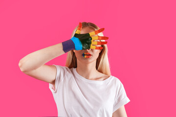 pretty caucasian blonde girl with lips and hands painted in rainbow flag. cover her face with hand. LGBT lesbian, gay. close up. isolated on the pink background. copy space.