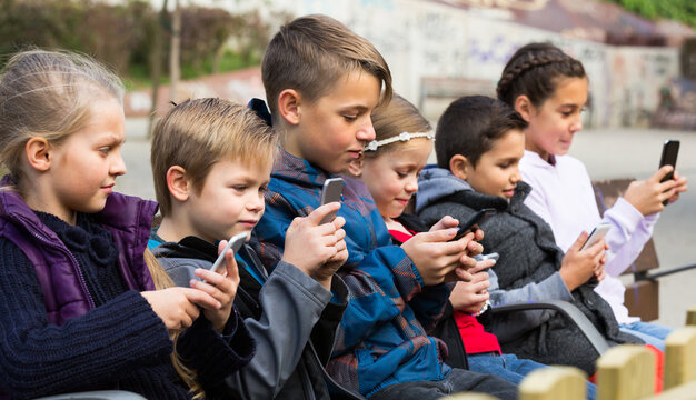 Group of children posing at urban street with mobile devices in sunny town