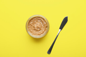Jar of tasty peanut butter and knife on color background