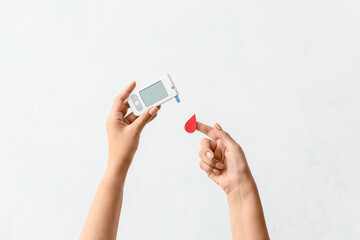 Female hands with glucometer and blood drop on light background. Diabetes concept