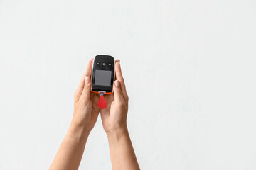Female hands with glucometer and blood drop on light background. Diabetes concept