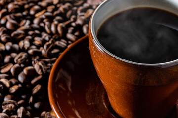 カップに入った湯気の立つ熱いコーヒーと背景のコーヒー豆