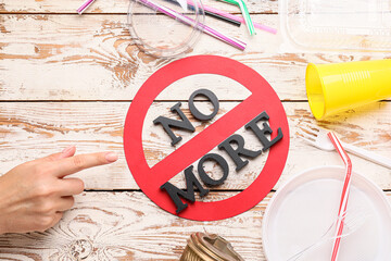 Female hand, plastic tableware and stop sign with text NO MORE on wooden background. Ecology concept