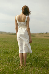 Nice picnic on the grass. Young beautiful woman in the middle of green field. Summer landscape, good weather. Windy day with sun and clouds. Cotton white suit eco style.