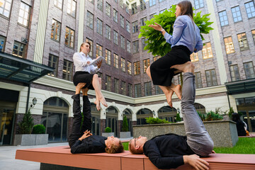 Acroyoga concept with four people, two base men lay on bench at hold at feet two flyer girls during...
