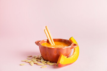 Tasty pumpkin cream soup in pot on color background