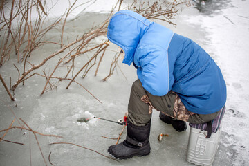 the fisherman sits on a box and waits for a bite on a winter day