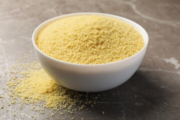 Bowl with raw couscous on gray background