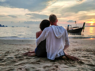 Sunset, sandy beach, couple in love sitting in an embrace at sunset on the beach on vacation