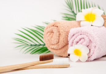 Obraz na płótnie Canvas Bamboo toothbrushes with towels in a wicker wooden basket and palm leaves and plumeria flower with copy space on white background. Spa, healthy lifestyle and ecology concept.