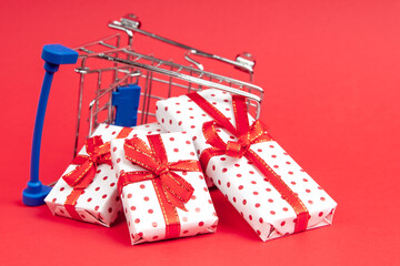 An overturned grocery cart full of gifts on a red background with copy space.  Concept for christmas, holidays, discounts and shopping.