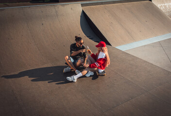 Young couple hangout in skate park while sitting on skateboard.