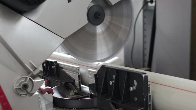 Factory industry worker cutting polypropylene pipe with circular saw. Warehouse of polypropylene pipes. Workshop with extruders for producing plastic pipes.