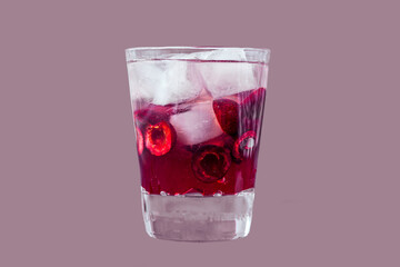 Fresh cherry cocktail. A cocktail with gin or vodka, cherry syrup and pieces cherry and ice in a whiskey glass. Glass of drink isolated on purple background