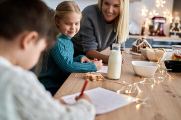 Mother helping children to write letter to Santa Claus
