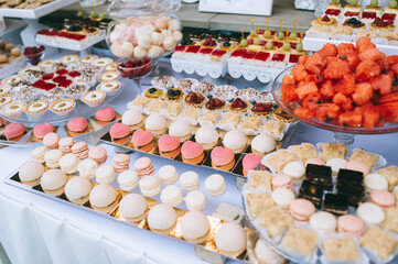 Wedding candy bar with different colored bright cupcakes, macaroons, cakes, jelly and fruits.