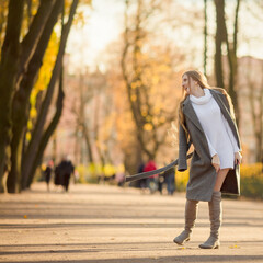 Obraz premium Happy young woman walks in the autumn park. An attractive woman with light brown hair and a gray coat is walking down the alley. Beautiful autumn mood. Fall season.