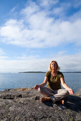 Fototapeta na wymiar Seinor woman relaxing and meditating outdoors by the sea on a summer day