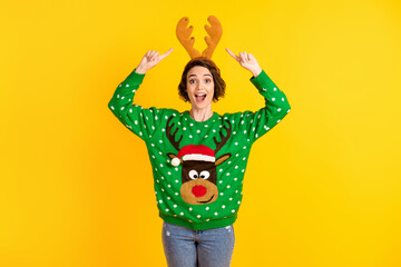 Astonished crazy girl deer green x-mas sweater point finger reindeer headband receive gift present theme costume party wear denim jeans isolated bright shine color background