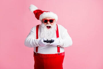 Portrait of his he nice cheerful cheery glad focused bearded fat guy Santa father playing console station contest network battle competition air blow wind contest isolated pink pastel color background © deagreez