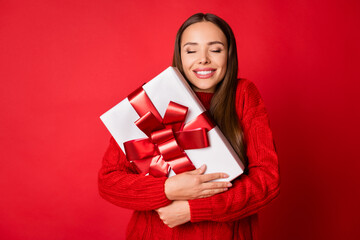 Photo of positive girl hug christmas x-mas gift box wear sweater isolated over bright shine red...