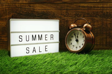 Summer Sale text in light box and alarm clock on wooden background