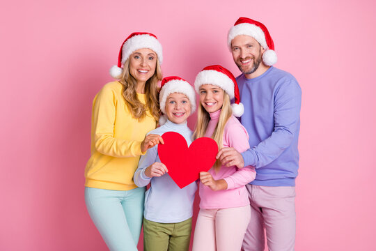 Photo of x-mas winter december people mom dad two little kids hold paper card heart wear santa claus cap isolated pink color background