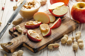 Cut board with apple slices with peanut butter on white wooden kitchen table