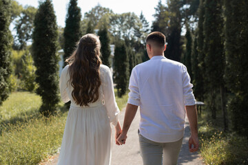Fototapeta premium a guy and a girl in white clothes hold hands and walk in the park