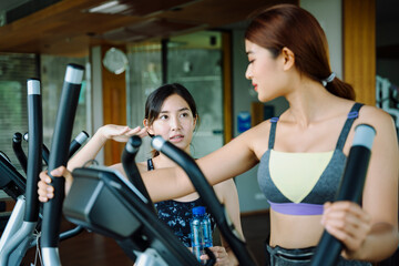 Fototapeta premium Beautiful woman work out on machine with trainer at gym.