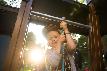 Obraz premium Smiling boy swinging on a rope at a playground. Happy child boy in sunlight