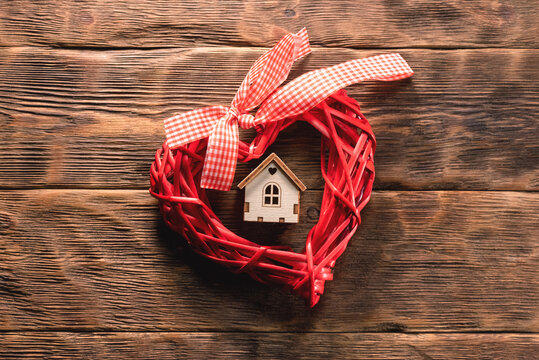 Home care concept. Cosiness. House A red heart toy and small house on the wooden table background top view.