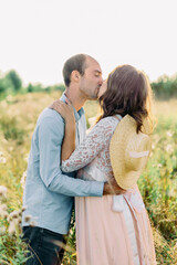 pregnant couple kissing at sunset among the grass. Blurred background. Flying seeds