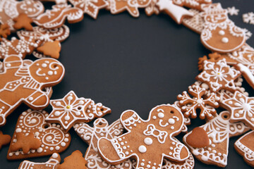 Christmas wreath made from gingerbread cookies with icing and confectionery mastic snowflakes on black background with space for text. Holiday food, homemade baking, Christmas and New Year traditions.