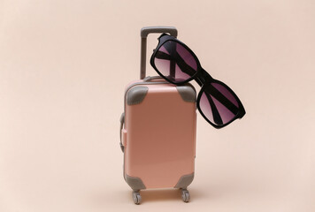 Travel or trip concept. Mini plastic travel suitcase with sunglasses on beige background.