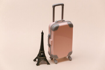 Traveled to Paris. Mini plastic travel suitcase and statuette of the Eiffel Tower on beige background.