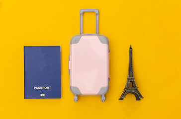 Traveled to Paris. Mini plastic travel suitcase and statuette of the Eiffel Tower, passport on yellow background. Top view. Flat lay